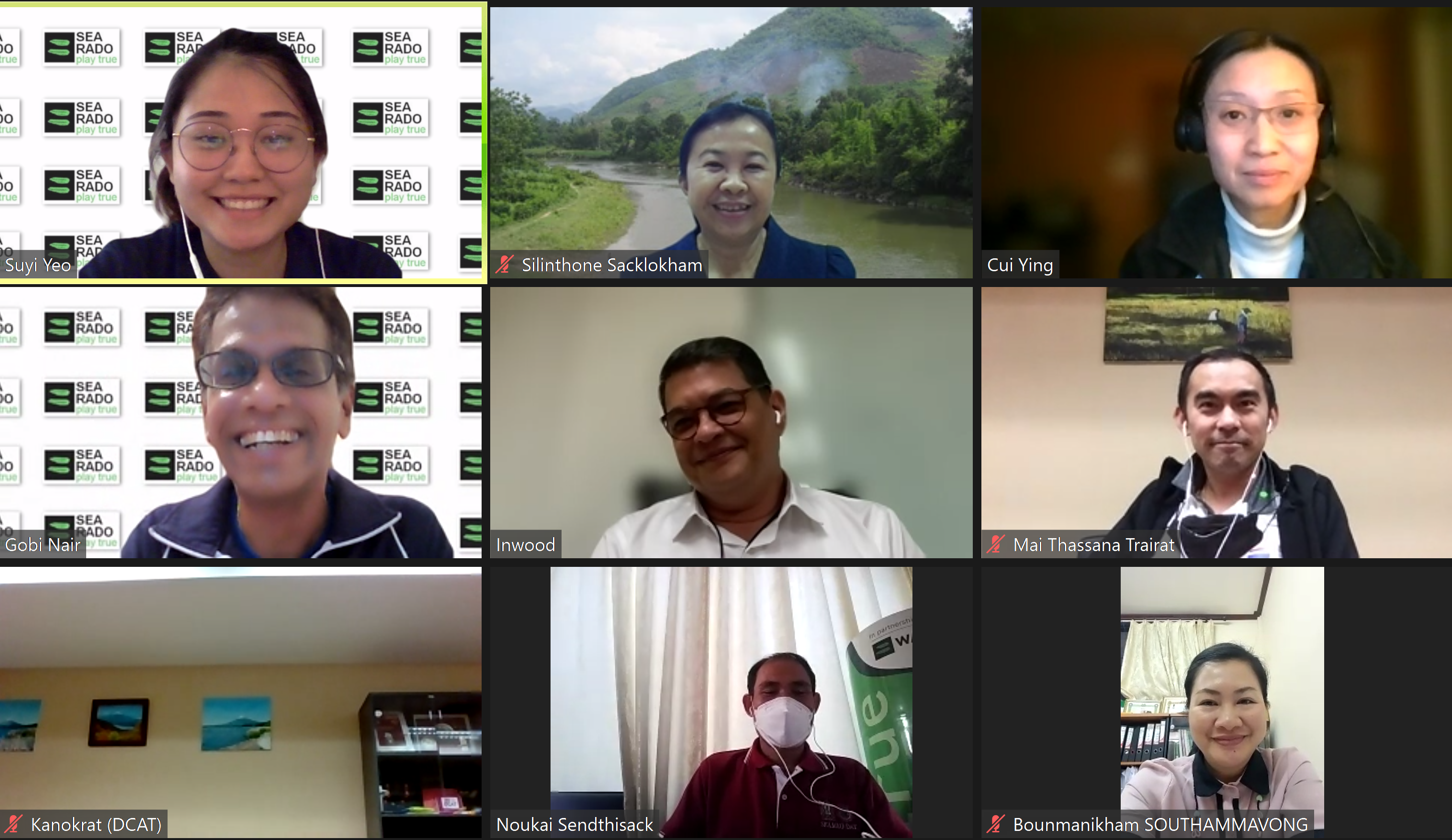 Nine-person video call grid with blurred faces; some muted, with logos and a river landscape background.